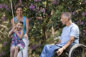 Man with spinal cord injury in wheelchair watching his daughter on swing along with wife